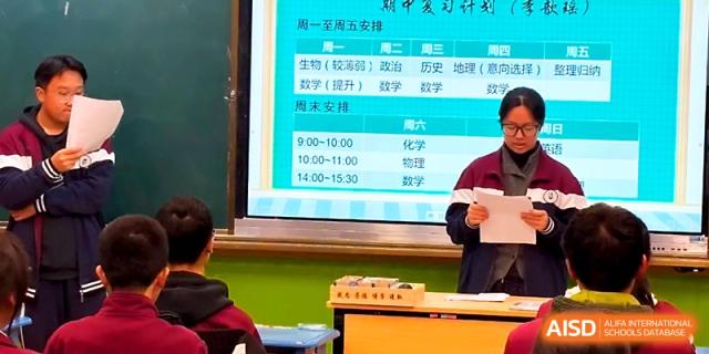 A student stands at a podium in front of a class schedule on a digital screen to lead a morning meeting at Yangzhou Shuren High School.
