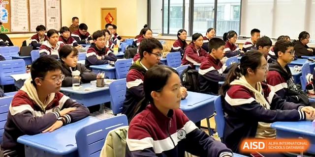 Students in maroon uniforms sit at blue desks, looking toward the front of the room during a group lecture at Yangzhou Shuren High School.
