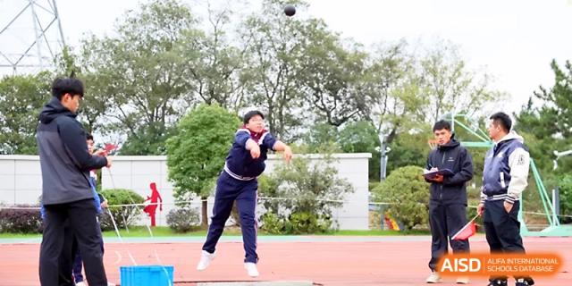 A student throws a shot put with great effort during a competitive outdoor sports meet held at Yangzhou Shuren High School.