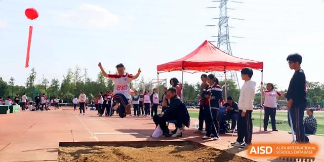 An athlete lands in the sand pit during a long jump attempt as spectators and officials watch the competition at Yangzhou Shuren High School.