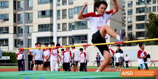 A male student in a red and white uniform successfully clears the bar during a high jump competition at the sports meet for Yangzhou Shuren High School.