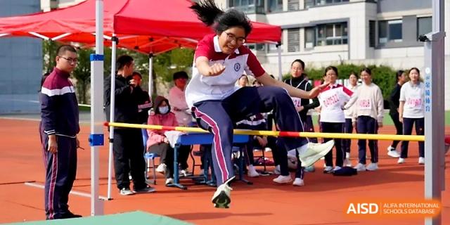 A young girl in a white shirt clears the high jump bar with great form during the annual school sports day at Yangzhou Shuren High School.