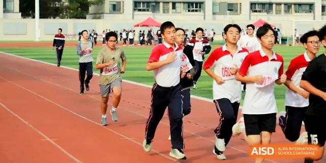 Three boys in athletic gear race toward the camera during a middle-distance running event on the track at Yangzhou Shuren High School.