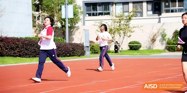 Two female runners compete side-by-side during a relay race under the bright sun on the campus of Yangzhou Shuren High School.