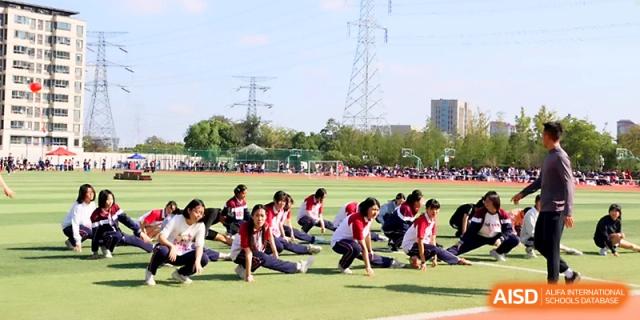 A group of students in matching tracksuits performs a synchronized stretching routine on the green field at Yangzhou Shuren High School.