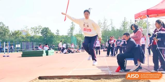 A student athlete leaps into the air for a long jump attempt during a field event on a sunny day at Yangzhou Shuren High School.