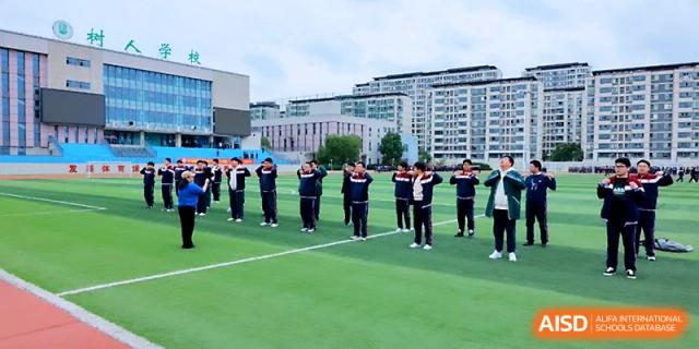 A group of students in dark uniforms stands in formation on the green sports field for a school ceremony at Yangzhou Shuren High School.