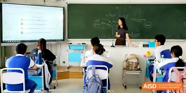 A teacher stands at the front of a classroom using a digital screen and chalkboard to lead a lesson for students at Yinchuan No.1 High School.