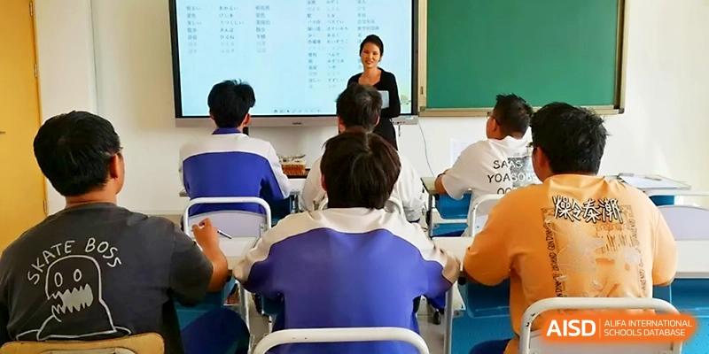 A smiling teacher engages with a class of students wearing blue uniforms while presenting a digital lesson at Yinchuan No.1 High School.
