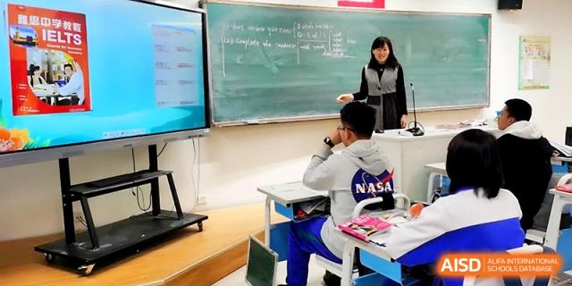 A female teacher gestures toward a chalkboard and digital screen while leading a lesson for an attentive student at Yinchuan No.1 High School.