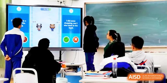 Two students stand before a large digital monitor, participating in a language learning activity during class at Yinchuan No.1 High School.