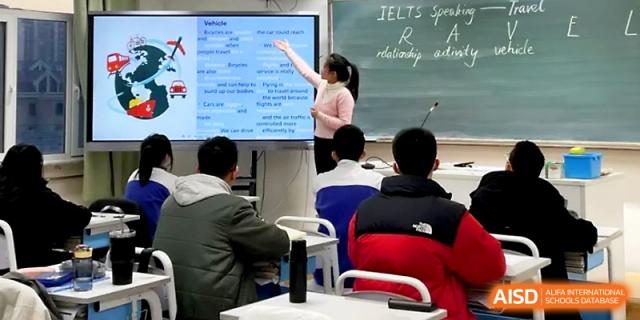 A teacher points to a digital whiteboard displaying an IELTS speaking lesson to a class of focused students at Yinchuan No.1 High School.