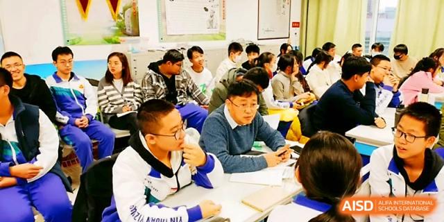 A teacher leans over a desk to provide personalized guidance to a group of students during a workshop at Yinchuan No.1 High School.