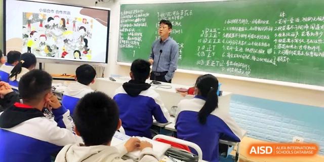 A male teacher stands before a chalkboard covered in writing, explaining a lesson to his attentive students at Yinchuan No.1 High School.