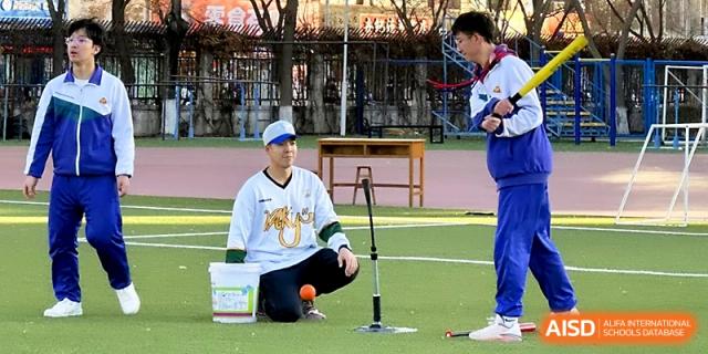 A coach in a baseball jersey kneels on the green field to instruct a student during an outdoor sports practice session at Yinchuan No.1 High School.