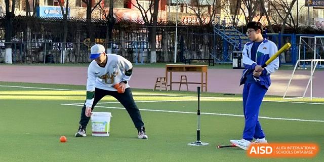 A baseball coach reaches into a bucket of balls while setting up a batting tee for students on the athletic field at Yinchuan No.1 High School.