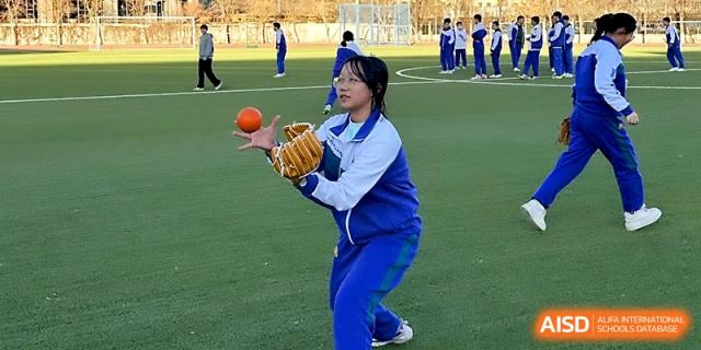 A female student in a blue tracksuit focuses on catching a baseball with her glove during an outdoor PE class at Yinchuan No.1 High School.