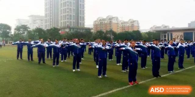 Students stand in a wide formation on the green grass, practicing rhythmic movements during an outdoor event at Yinchuan No.1 High School.