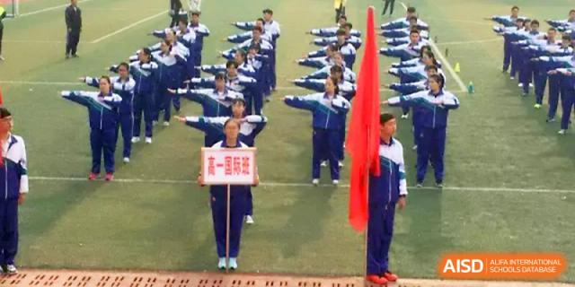 Students participate in a formal ceremony on the track, holding a school sign and a red flag for a procession at Yinchuan No.1 High School.