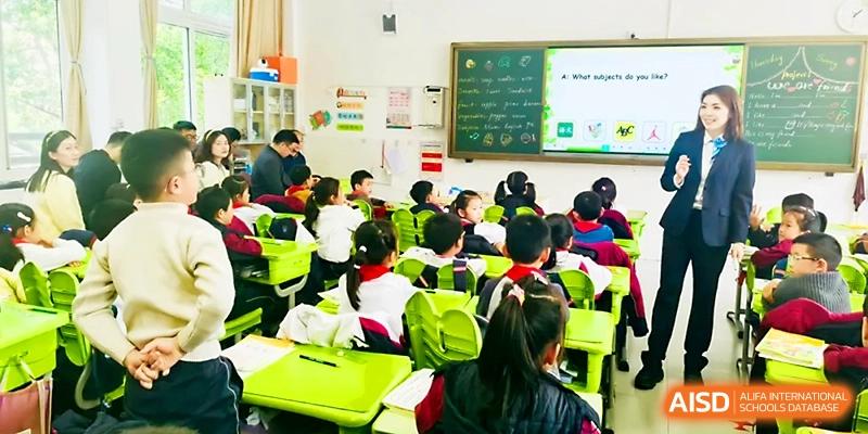 A classroom full of students in uniforms sits at bright green desks, focused on their teacher at Zhangjiagang IVY Experimental School.