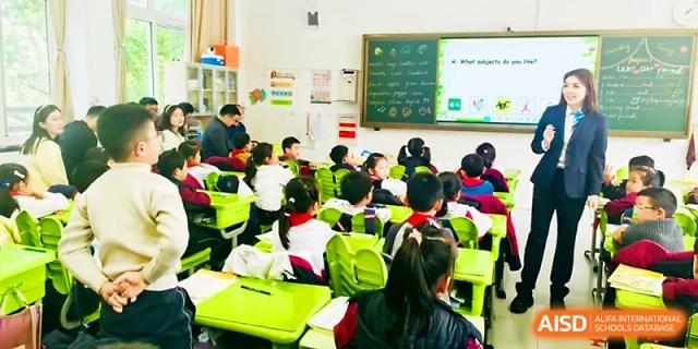 A classroom full of students in uniforms sits at bright green desks, focused on their teacher at Zhangjiagang IVY Experimental School.