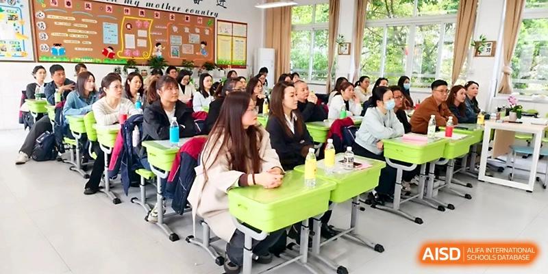 A group of adults sits at student desks, participating in a school community event or training at Zhangjiagang IVY Experimental School.