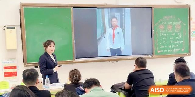 A teacher points to a video on a screen featuring a student speaker during an interactive session at Zhangjiagang IVY Experimental School.