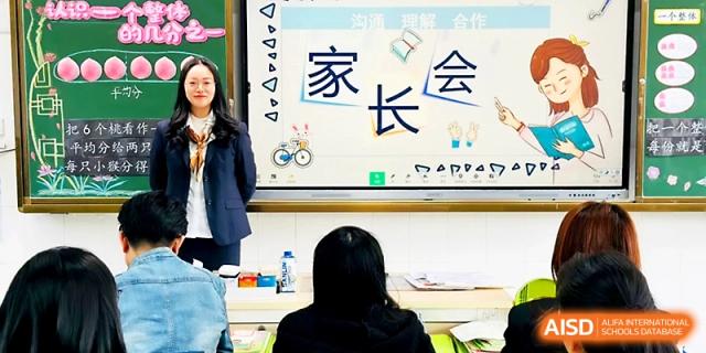 A teacher stands at the front of a classroom during a parent-teacher meeting with a welcoming screen at Zhangjiagang IVY Experimental School.