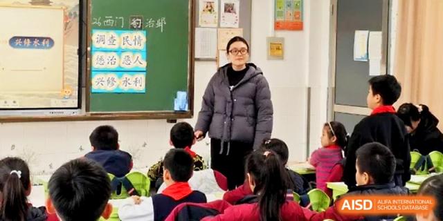 A female teacher in a grey jacket leads a class discussion with primary students at Zhangjiagang IVY Experimental School.