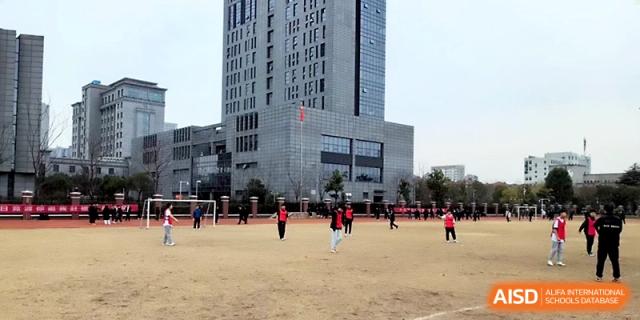 Students participate in outdoor exercise on a field in front of a modern school building at Zhangjiagang IVY Experimental School.