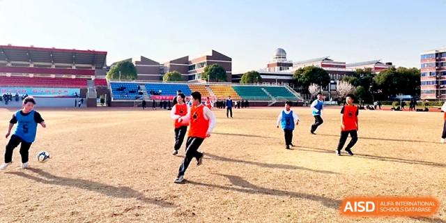 Several students in red and blue athletic vests run across an outdoor track during a sports event at Zhangjiagang IVY Experimental School.