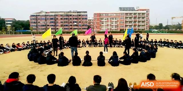 A large group of students and teachers gather in a circle on the field for an outdoor meeting at Zhangjiagang IVY Experimental School.