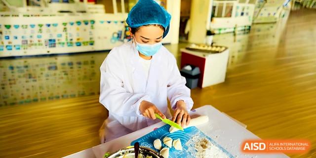 A cafeteria worker in a white uniform and mask prepares fresh dumplings in the kitchen at Zhangjiagang IVY Experimental School.