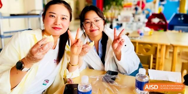 Two staff members smile and give peace signs while taking a break in the dining hall at Zhangjiagang IVY Experimental School.