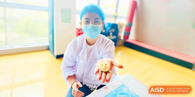 A kitchen staff member proudly displays a handmade baozi bun while wearing protective gear at Zhangjiagang IVY Experimental School.