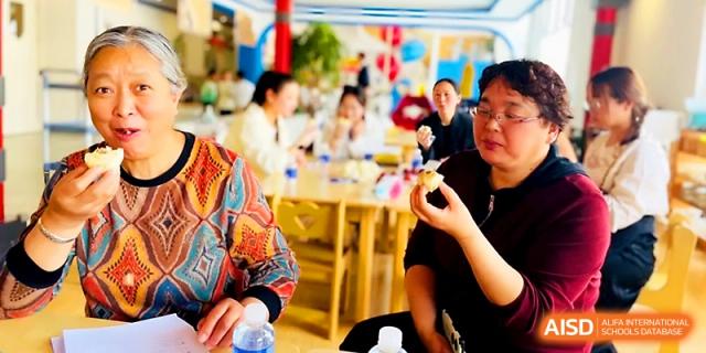 Students and teachers sit together at wooden tables enjoying a meal in the bright cafeteria at Zhangjiagang IVY Experimental School.