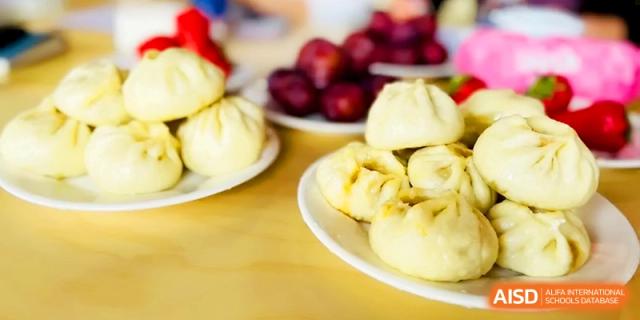 A close-up shot shows plates of freshly steamed white baozi buns ready for student meals at Zhangjiagang IVY Experimental School.