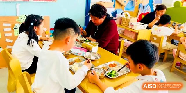 Students sit at long tables in the cafeteria, focused on eating their nutritious lunch at Zhangjiagang IVY Experimental School.