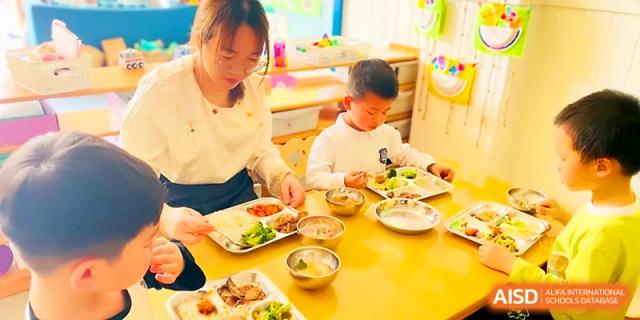 A teacher assists a young student with their meal in the school's colorful dining area at Zhangjiagang IVY Experimental School.