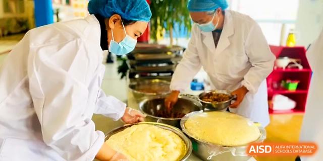 Staff members in protective clothing prepare large batches of dough in the school kitchen at Zhangjiagang IVY Experimental School.