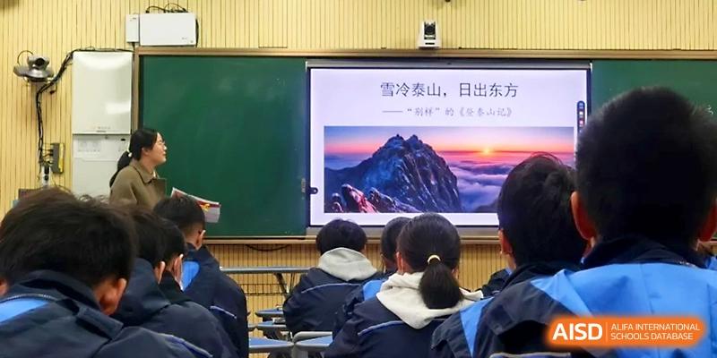 Students watch a presentation featuring a scenic mountain sunrise on a large digital screen in class at Zhejiang ZhouShan High School.