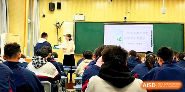 A teacher stands by a whiteboard while students focus on a lesson during a bright daytime class session at Zhejiang ZhouShan High School.