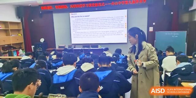 A teacher presents a detailed lecture slide to a large, attentive group of students in a modern classroom at Zhejiang ZhouShan High School.