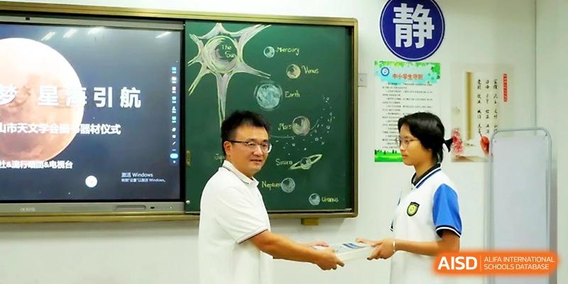 A teacher presents an award or book to a student in front of a chalkboard featuring a hand-drawn solar system at Zhejiang ZhouShan High School.