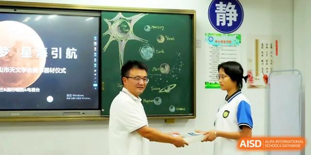 A teacher presents an award or book to a student in front of a chalkboard featuring a hand-drawn solar system at Zhejiang ZhouShan High School.