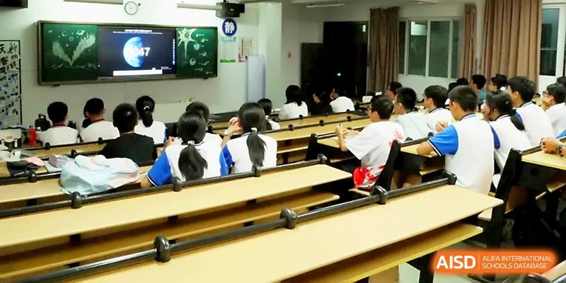 Students are seated in a tiered lecture hall, focusing on a digital screen during a specialized academic session at Zhejiang ZhouShan High School.