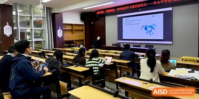 An empty lecture hall with rows of desks faces a bright screen displaying an educational presentation at Zhejiang ZhouShan High School.