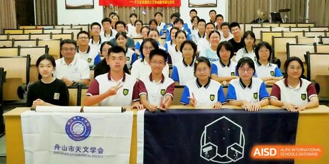 A large group of students in matching uniforms poses for a commemorative group photo in an assembly hall at Zhejiang ZhouShan High School.