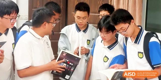 Three students collaborate and discuss the contents of a textbook during a study session in the classroom at Zhejiang ZhouShan High School.