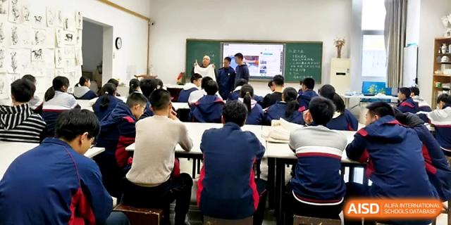 A teacher leads a discussion at the front of a classroom while students sit at white tables for a workshop at Zhejiang ZhouShan High School.